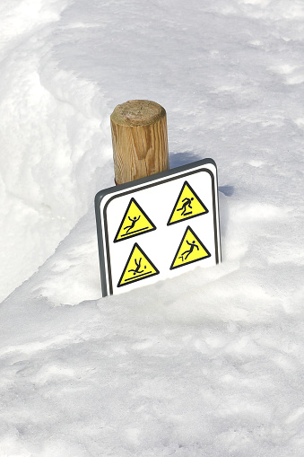 Fresh snow buries a warning sign with pictograms alerting of the danger of falling and slipping due to ice