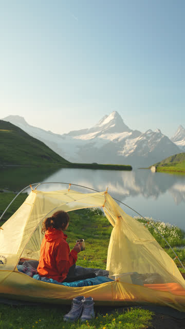 Woman drinking coffee in the tent near the idyllic lake in Swiss Alps