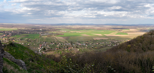 Panoramic picture from the Somló Hill to a village and agricultural fields on a cloudy day in springtime. Also there are some hills in the background.
