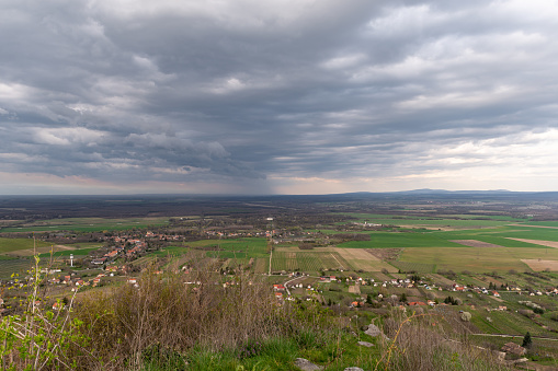 View from the Somló Hill to a village and agricultural fields on a cloudy day in springtime. There is heavy rain in the background.