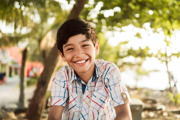 Happy Young Boy Smiling in a Sunny Outdoor Setting A portrait of a cheerful young boy with a beaming smile, enjoying a sunny day outdoors with a blurred background. small boys stock pictures, royalty-free photos & images