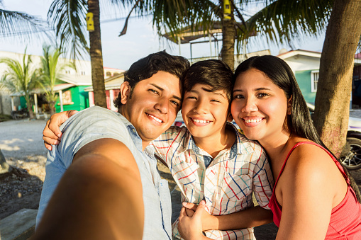 A cheerful family with a young boy sharing a joyful moment while taking a selfie outside on a bright sunny day.