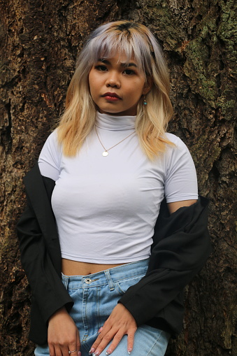 A front view portrait of a Filipino woman. She is wearing medium length multi colored hair, white t-shirt, jeans, and a black off the shoulder jacket.