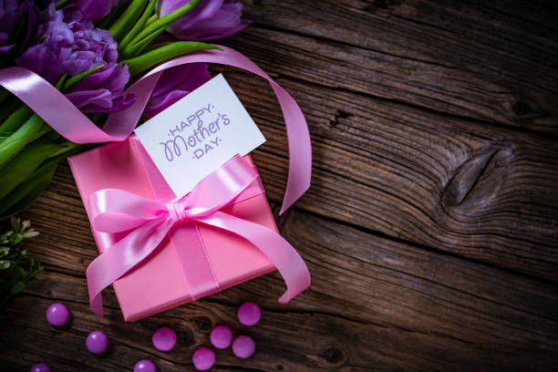 istock Mother's Day concept: pink gift box, tilips and candies on wooden table 2146458537