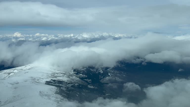 Snowed mountains covered with some flufly clouds. Guadalajara, Spain. Pilot POV. Forward aerial shot from an airplane cockpit. 4K.