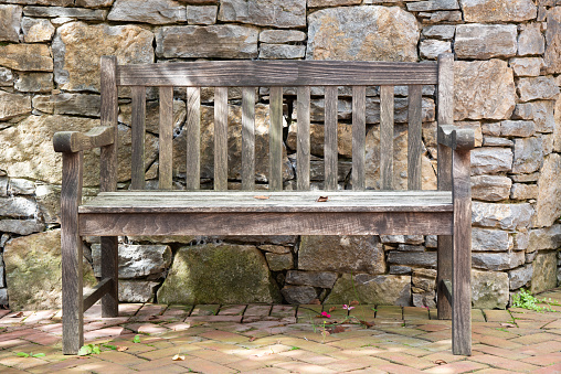 Empty, wooden park bench against a rock wall.