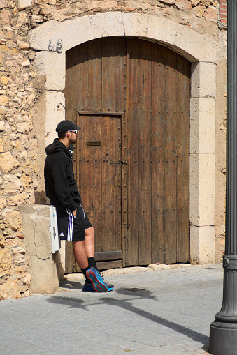 Tarragona, Spain - April 6, 2024: A moment of introspection captured in front of an old wooden door, where a man in casual attire reflects the fusion of the present with the past.