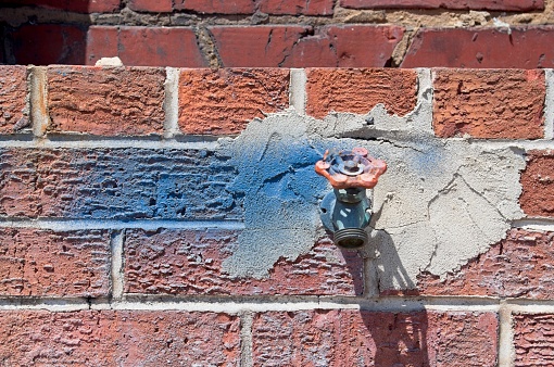Water spigot with blue paint on a brick wall