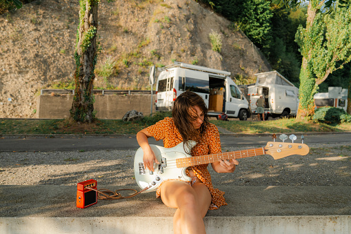 Woman playing bass guitar on the background of camper van in summer