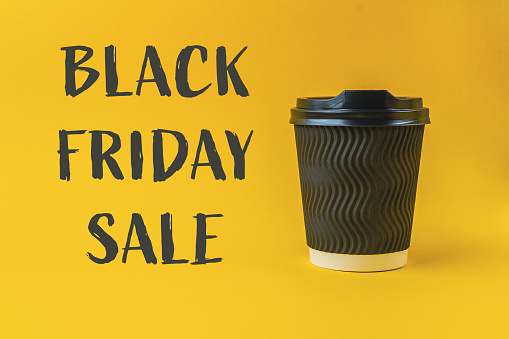 A black coffee cup sits on a yellow background with the words Black Friday Sale written below it. Concept of excitement and anticipation for the upcoming holiday shopping season