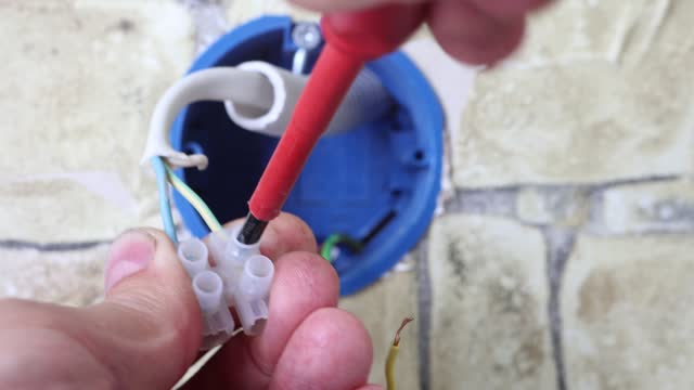Electrician connects wires with screw clamp fixing terminal block in electrical wiring box.