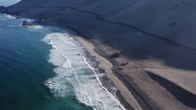 Single road cuts across sandy mountain slope at beach in coastal Chile