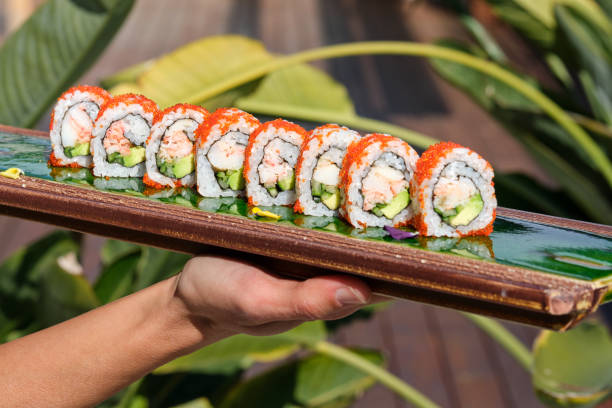 Crop faceless person holding tray with traditional sushi rolls