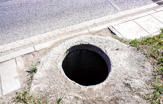 Open unsecured manhole on the side of an asphalt road. Dangerous pit on the road. Sewer well hatch on the street