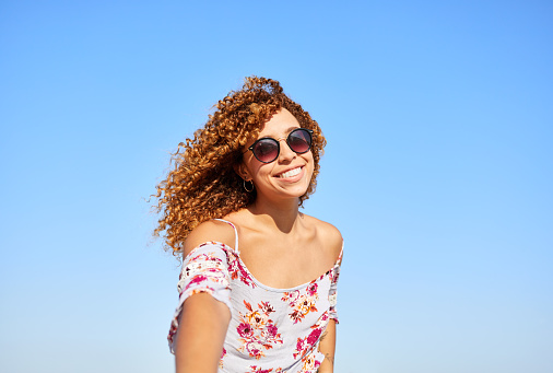 Cheerful and smiling young woman looking at the camera on a summer day. Blue sky in the background
