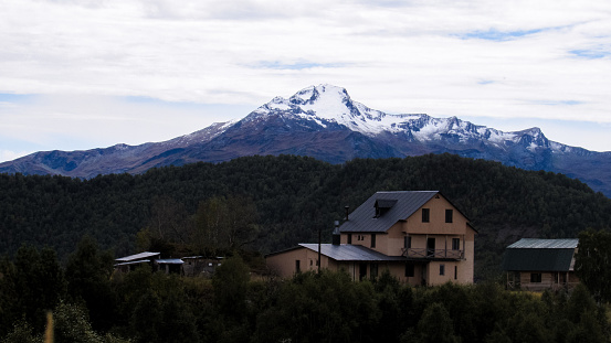 A house in a forest at a mountain range with a snowy mountain in the background. Located in the middle of the 4 days Mestia to Ushguli trek in the country of Georgia.