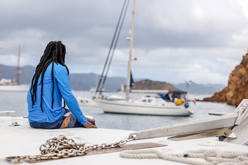 Tortola, British Virgin Islands - March 27, 2024: A deckhand sitting on the bow of a tour boat off the shores of Norman Island in the British Virgin Islands
