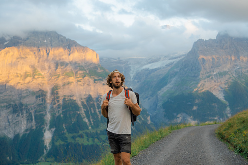 Serene man in cap  with backpack hiking in Swiss Alps at sunset in summer