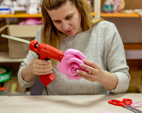 A woman in her workshop makes flowers using hot glue and a hairdryer
