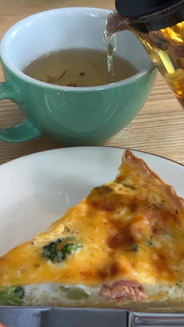 a close up of a pie on a plate with broccoli and a cup of tea in the background.