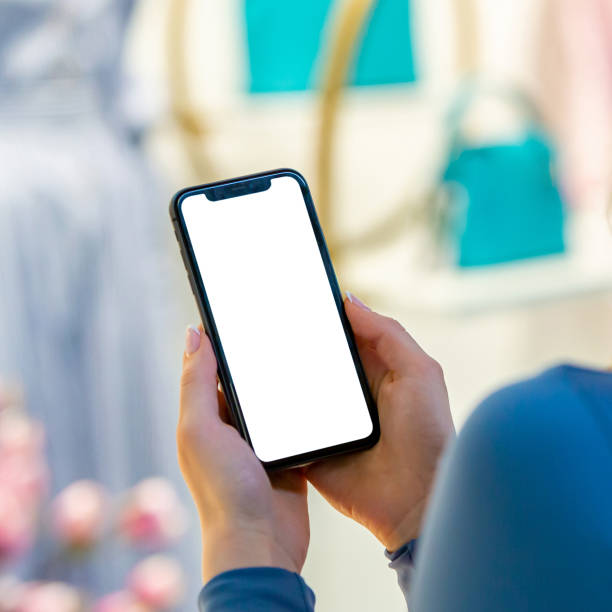 Phone blank white screen: In this adaptable image, a woman holds a smartphone with a blank screen in both hands, offering versatility for customization. Whether for showcasing app designs, digital artwork, or UI/UX mockups, this template provides ample space for creativity. Ideal for designers, marketers, and content creators seeking a clean and professional canvas to present their digital creations effectively.
