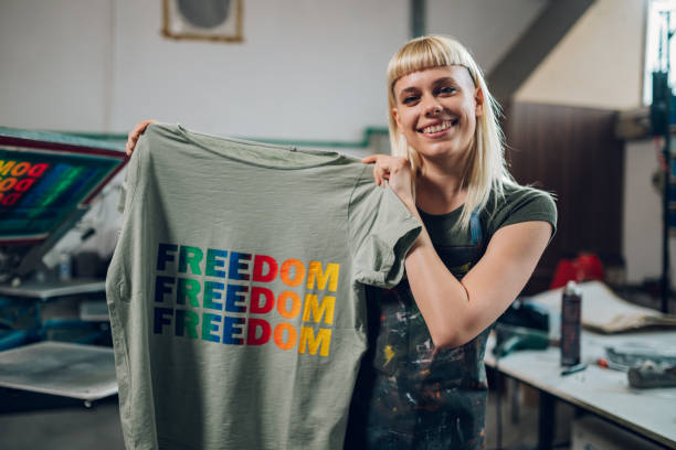 istock Smiling print shop worker showing silkscreen printed t-shirt at camera 2147087617