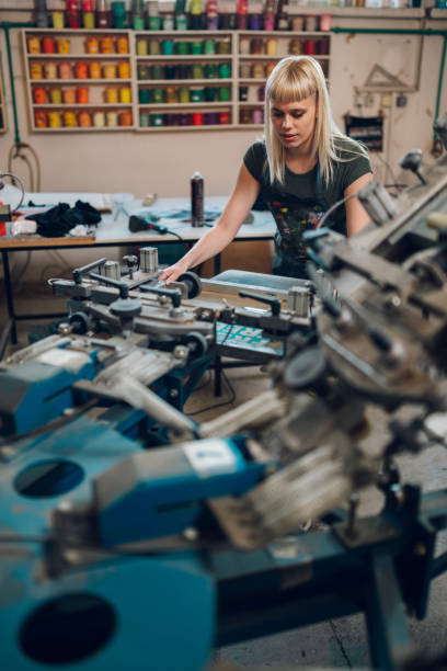 istock Graphic worker manipulating screen printing press at printing shop. 2147087623