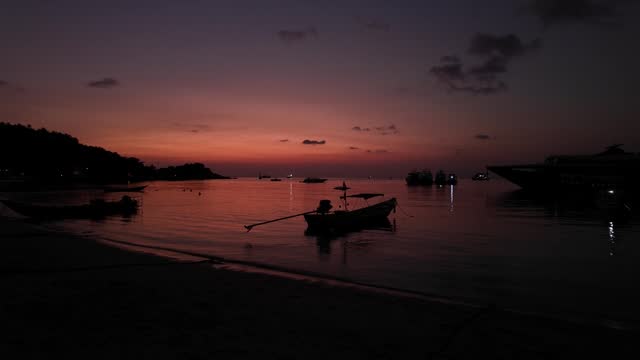 Multiple boats moored in sheltered beach on tropical island, shot during beautiful pink and orange sunset