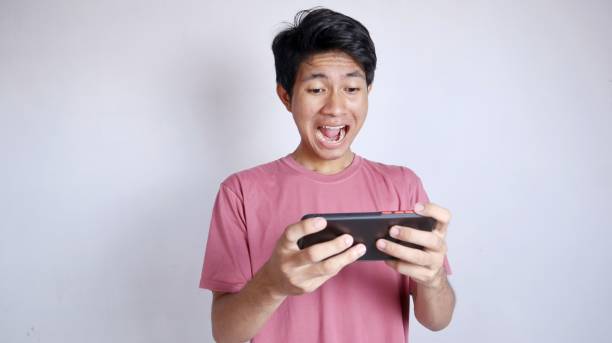 excited asian man playing games on smartphone on white background