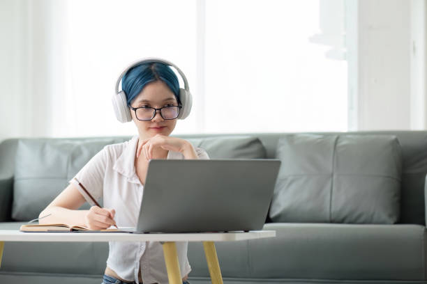 istock Happy young woman teenage wearing headphones writing note. student online learning class study online video call zoom teacher with laptop and book 2147405896