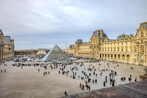 Paris, France - December 27, 2023:  Lot of tourists roaming outside Musee du Louvre with the pyramid, as viewed from an advantage point inside Musee du Louvre.  HDR encoded