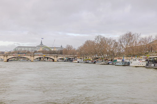 Paris, France - December 29, 2023:  Pont de la Concorde and Grand Palais as viewed from a Seine River cruise boat, with many boats docked alongside the river on a cloudy day.  HDR encoded