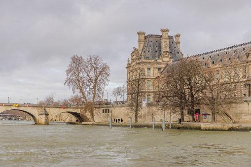 Paris, France - December 29, 2023:  Musee du Louvre and Pont Royal as viewed from a Seine River cruise boat on a cloudy day.  HDR encoded