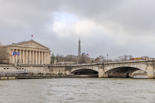 Paris, France - December 29, 2023:  Palais Bourbon, Eiffel Tower, and Pont de la Concorde as viewed from a Seine River cruise boat on a cloudy day.  HDR encoded