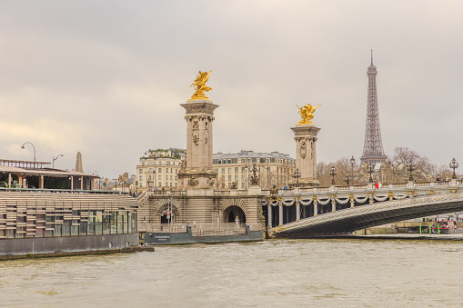 Paris, France - December 29, 2023:  Eiffel Tower and Pont Alexandre III as viewed from a Seine River cruise boat on a cloudy day.  HDR encoded
