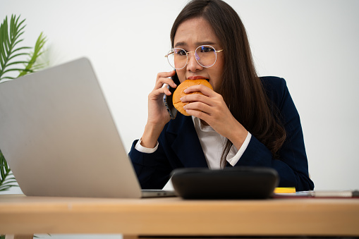 Busy and tired businesswoman eating Bread and milk for lunch at the Desk office and working to deliver financial statements to a boss. Overworked and unhealthy for ready meals, burnout concept.