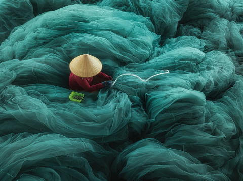 High angle view of a woman is knitting net on a large beautiful turquoise fishing net in Hon Ro dock, Nha Trang city, Khanh Hoa province, central Vietnam