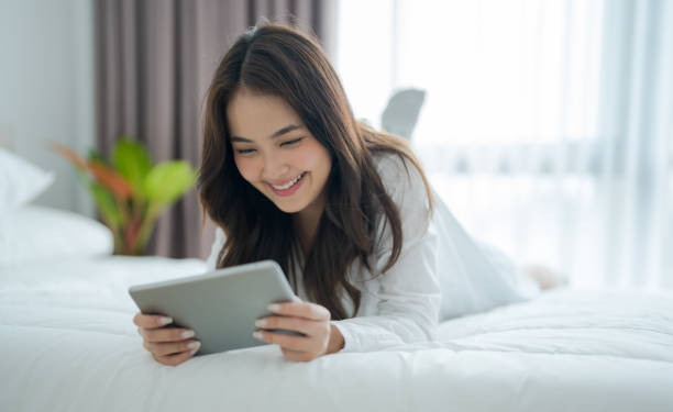 istock Girl lying in bed playing tablet computer in bedroom With a smiling face 2147486361
