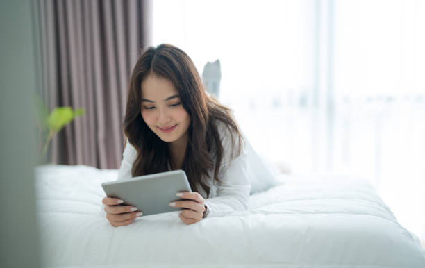 istock Girl lying in bed playing tablet computer in bedroom With a smiling face 2147486370