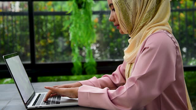 Muslim woman wear hijab work from home office typing laptop keyboard on wooden desk with office supply happy smiling face. Young Asian arabian muslim women working summary report business graph chart