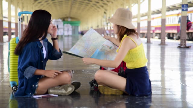 Asian young woman traveler friendship backpack looking maps brochure at railway station. Two Female travel passenger by plane tourist baggage. Happy Tourism trip women friends journey on vacation