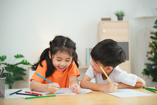 Two children are sitting at a table, drawing and smiling. Concept of joy and creativity, as the children are engaged in a fun activity together