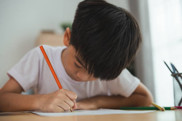istock A young boy is sitting at a desk and writing with a pencil. He is focused on his work and he is in a serious mood. Concept of a child learning and practicing their writing skills 2147494525