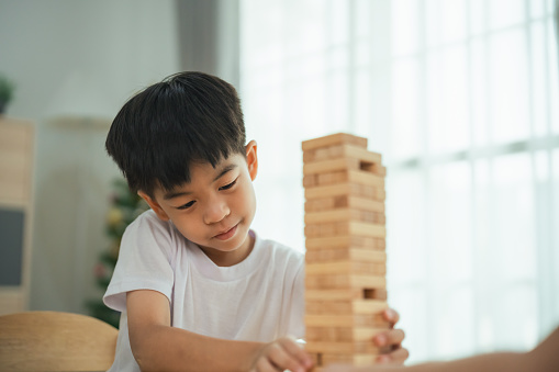 A young boy is playing with a wooden block tower. He is focused on the game and he is enjoying himself
