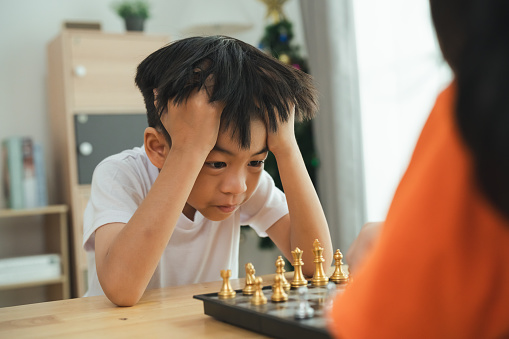 A boy is playing chess with another person. He is looking at the board with a sad expression