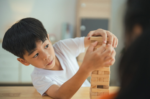 A young boy is playing with a wooden block tower. He is focused on the tower and he is enjoying himself