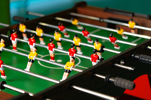 A detailed view of a foosball table featuring miniature players in red and blue colors competing in a fast-paced game. The figures are strategically positioned on metal rods, aiming to score goals by moving back and forth across the table.