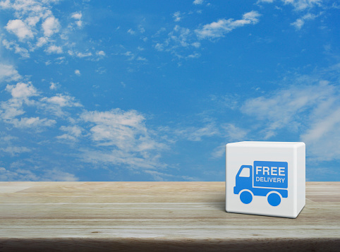 Free delivery truck icon on white block cube on wooden table over blue sky with white clouds, Business transportation service concept