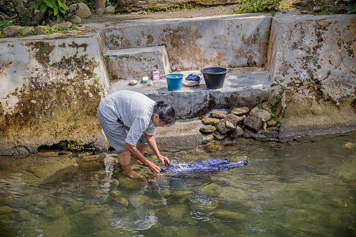 Bukit Lawang, Sumatra, Indonesia - January 23th 2024: Mature woman washing her laundry in the river which runs through the village