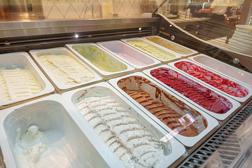 A variety of gelato flavors are neatly arranged in a display case, showcasing vibrant colors and tempting textures that indicate a rich, creamy dessert experience at an Italian ice cream parlor.
